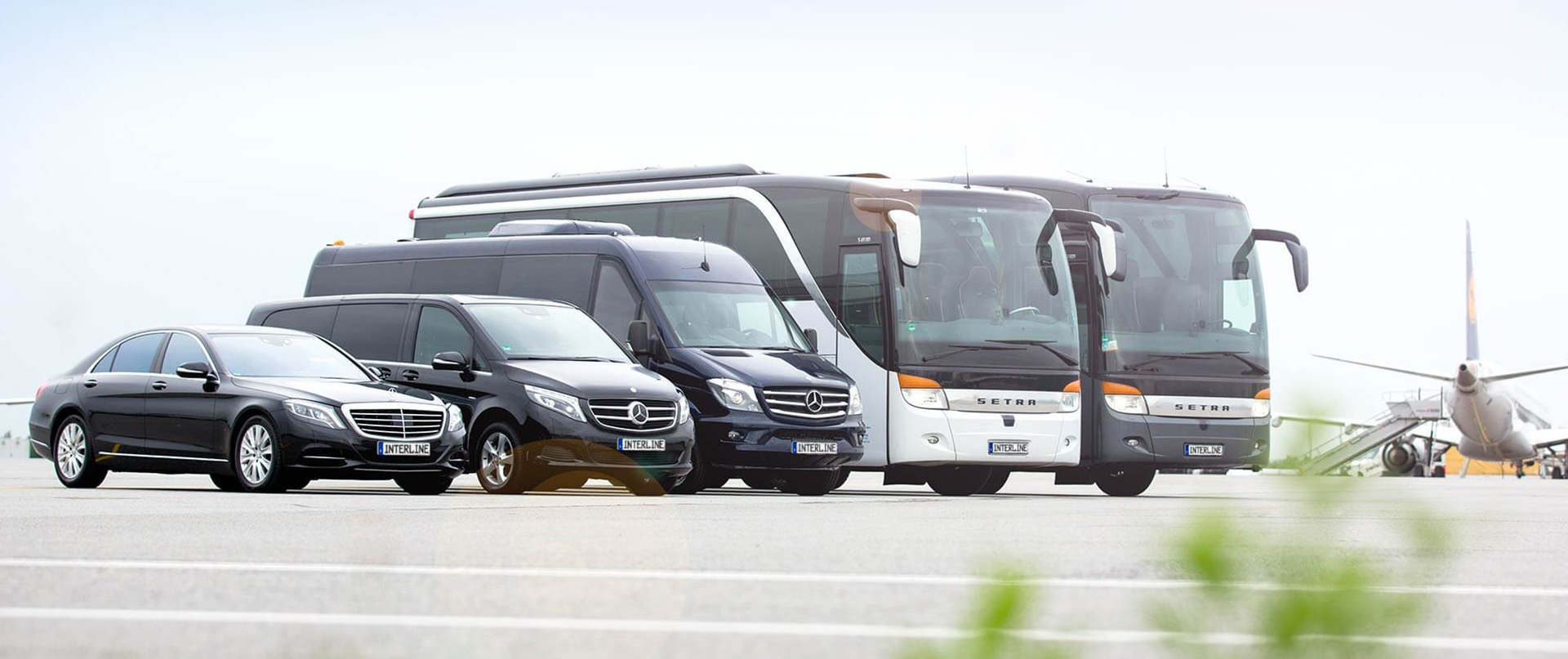 Reisebusse und Minivans auf dem Rollfeld vor einem Flugzeug.