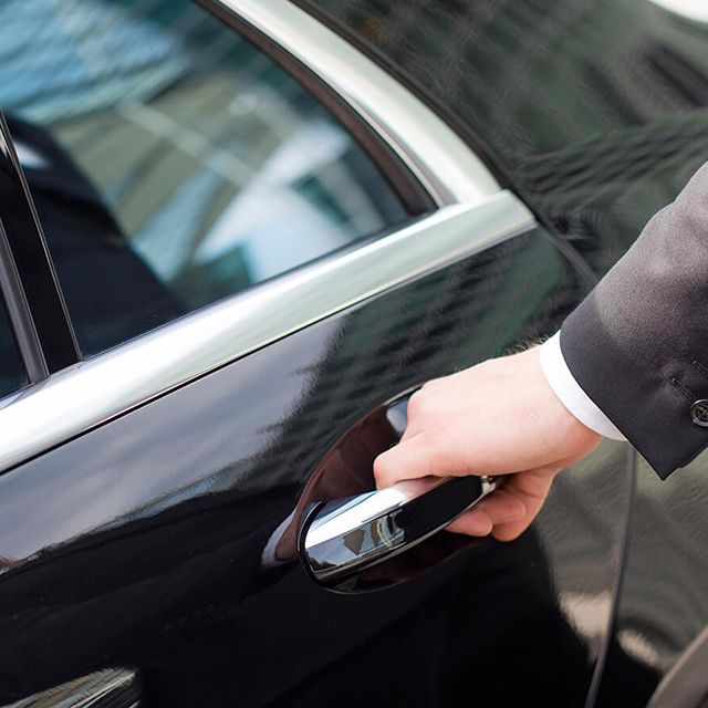 The hand of a chauffeur on the door handle of a limousine.