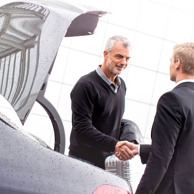 A chauffeur is shaking hands with a passenger besides a limousine.
