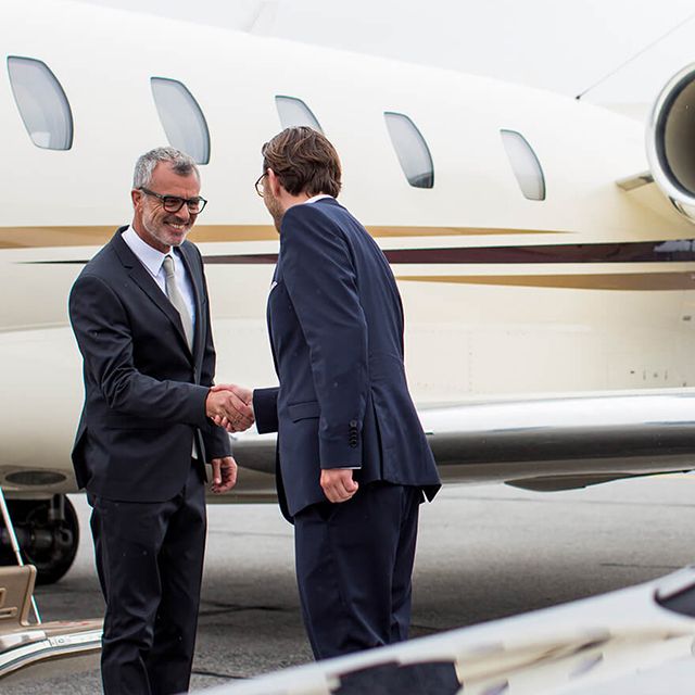 Ein Chauffeur begrüßt einen Fahrgast vor einem Business-Jet.